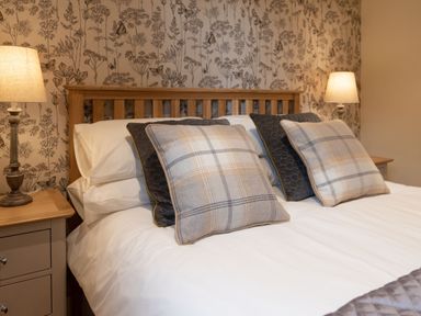 A bedroom with a wooden bed frame two bedside tables with lamps and decorative pillows at Larchwood Lodge in Ellon