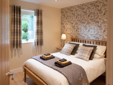A bedroom with a wooden bed with pillows and folded towels on a quilted runner at Larchwood Lodge in Ellon