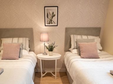 A bedroom with two single beds separated by a round white table with a lamp and plant at Larchwood Lodge in Ellon