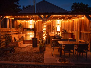 An outdoor wooden patio with string lights a seating area a dining table grill and plants at Larchwood Lodge in Ellon