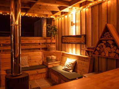 A wooden seating area with cushions a basket a plant and stacked firewood at Larchwood Lodge in Ellon