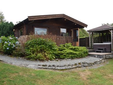 A wooden cabin with a gravel path garden shrubs and a hot tub gazebo at Hillside View in Rhayader