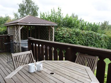A wooden deck with a table and chairs and a gazebo with hot tub behind at Hillside View in Rhayader