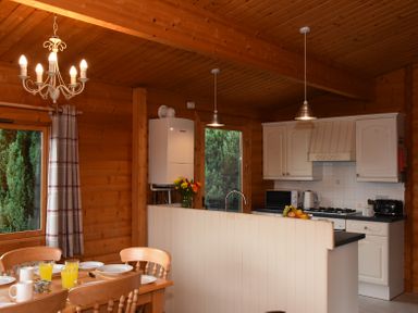 A kitchen and dining area with wooden walls and ceiling a dining table set with glasses and plates at Hillside View in Rhayader