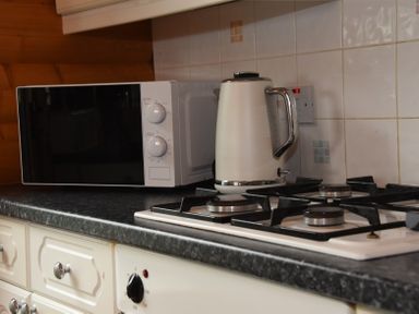A kitchen countertop with a microwave oven a white electric kettle and a gas stove at Hillside View in Rhayader