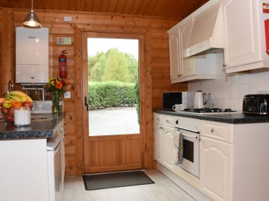 A kitchen with white cabinets and a wooden door opening outside at Hillside View in Rhayader