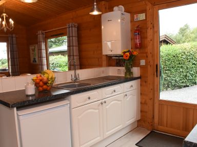 A kitchen with a sink fruit bowl flowers and a door leading outside at Hillside View in Rhayader