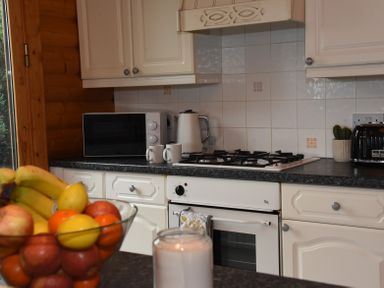 A kitchen countertop with a microwave kettle two mugs a toaster stove oven a bowl of fruit and a candle at Hillside View in Rhayader