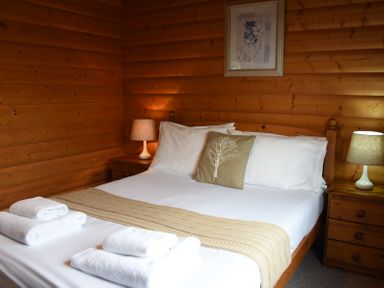 A bedroom with a bed white linen beige throw and towels on a wooden bedframe with bedside tables and lamps at Hillside View in Rhayader