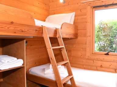 A wooden bunk bed with white bedding and towels near a window in a wooden room at Hillside View in Rhayader
