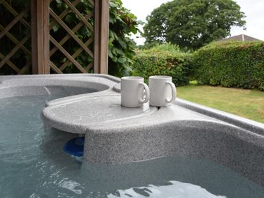 Two white mugs on the edge of a hot tub with water and greenery in the background at Hillside View in Rhayader