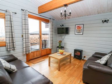 A living room with two leather sofas a wooden coffee table a wall-mounted TV and sliding glass doors at Snowy Owl Lodge in Rhayader
