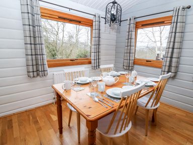A dining room with a wooden table set for four near windows with plaid curtains at Snowy Owl Lodge in Rhayader