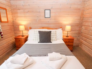 A bedroom with a double bed two bedside tables with lamps towels on the bed and wooden walls at Snowy Owl Lodge in Rhayader