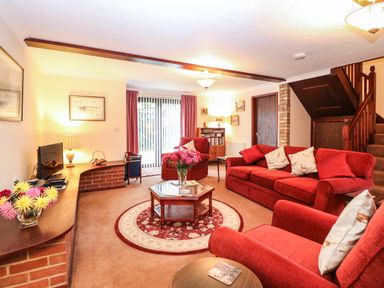 A living room with red sofas a round rug and a glass top coffee table at Walnut Tree Cottage in Catfield