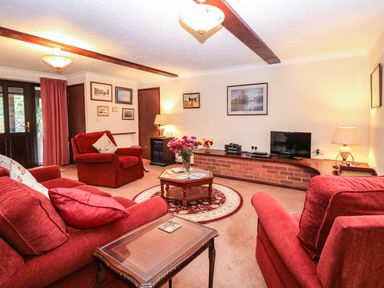 A living room with red sofas armchairs a coffee table and a television at Walnut Tree Cottage in Catfield