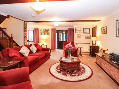 A living room with red sofas a wooden coffee table flowers and framed pictures at Walnut Tree Cottage in Catfield