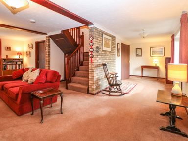 A living room with a red sofa wooden rocking chair a staircase and tables with lamps at Walnut Tree Cottage Catfield