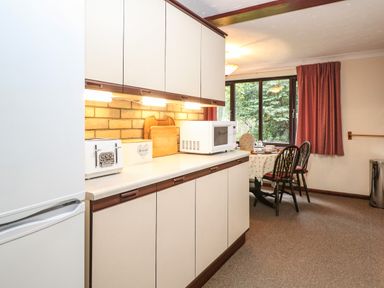 A kitchen with a countertop holding a toaster bread box microwave and cutting boards and a dining table by a window with chairs at Walnut Tree Cottage in Catfield