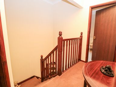 A staircase with wooden railing next to a hallway with a wooden door and a wooden table at Walnut Tree Cottage in Catfield