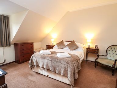 A bedroom with a double bed two bedside tables with lamps a wooden dresser an armchair and a window with curtains at Walnut Tree Cottage in Catfield
