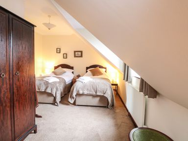 A bedroom with two single beds bedside tables lamps wardrobe and sloped ceiling at Walnut Tree Cottage in Catfield
