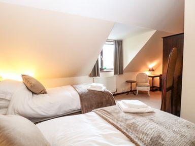 A bedroom with two single beds towels on beds a window with curtains a chair and a lamp at Walnut Tree Cottage in Catfield