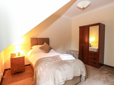 A bedroom with a single bed nightstand with a lamp wooden wardrobe and a small covered bench at Walnut Tree Cottage in Catfield