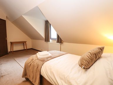 A bedroom with a bed pillow a blanket and a small wooden table under a window at Walnut Tree Cottage in Catfield