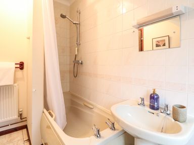 A bathroom with a bathtub with shower curtain and shower head next to a sink with soap dispenser at Walnut Tree Cottage in Catfield