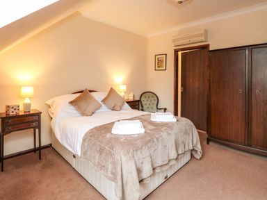 A bedroom with a double bed with pillows and folded towels two bedside tables with lamps an armchair a wardrobe and an open door at Walnut Tree Cottage in Catfield