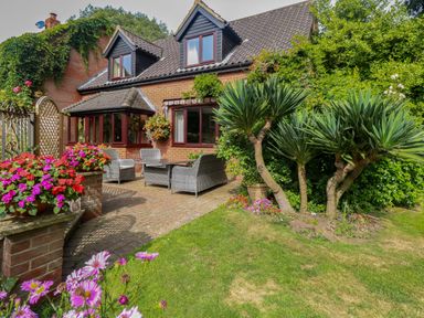 A garden patio with wicker chairs and table surrounded by flowers and plants at Walnut Tree Cottage in Catfield