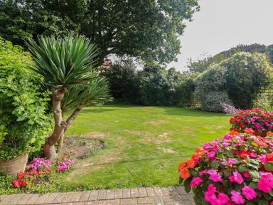 A garden with green grass flowering plants and bushes at Walnut Tree Cottage in Catfield