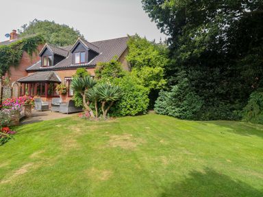 A brick house with a patio and garden furniture surrounded by plants and grass at Walnut Tree Cottage in Catfield