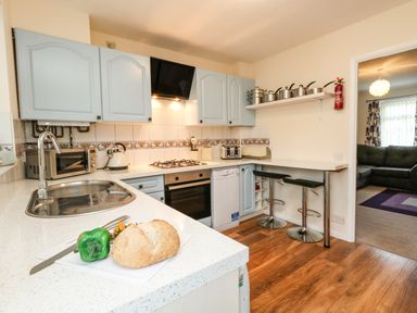 A kitchen with white countertops blue cabinets a sink and stove a loaf of bread and green pepper on the counter at Kingfisher Cottage in Weymouth