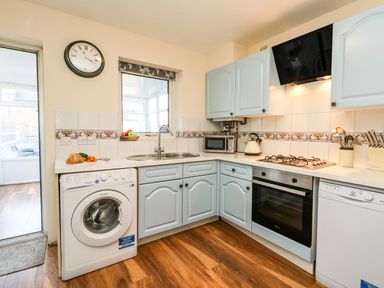 A kitchen with blue cabinets, washing machine, oven, dishwasher, microwave, kettle, sink, and wall clock at Kingfisher Cottage in Weymouth