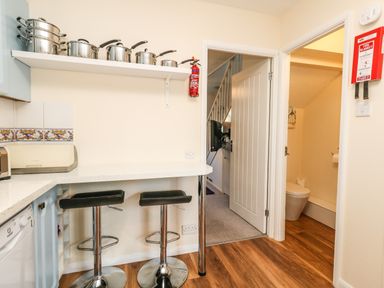 A kitchen with pots on a shelf and two black bar stools at Kingfisher Cottage in Weymouth