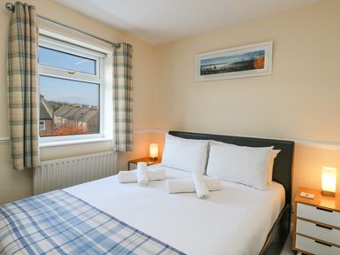 A bedroom with a bed covered with white sheets and rolled towels next to a window with plaid curtains at Kingfisher Cottage in Weymouth