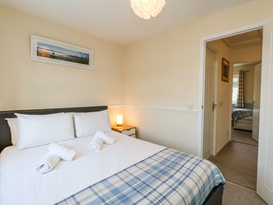 A bedroom with a bed white pillows and a plaid blanket a framed picture on the wall and a bedside table with a lamp at Kingfisher Cottage in Weymouth