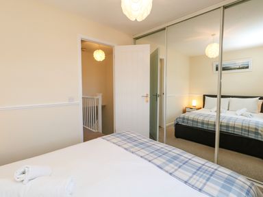 A bedroom with a bed covered by white sheets and a blue checked blanket with rolled towels on top at Kingfisher Cottage in Weymouth