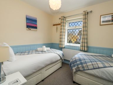 A bedroom with two single beds with plaid blankets and a window with plaid curtains at Kingfisher Cottage in Weymouth
