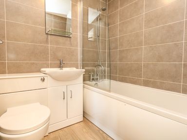 A bathroom with a toilet sink cabinet bathtub and tiled walls at Kingfisher Cottage in Weymouth