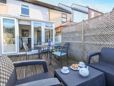 An outdoor patio area with wooden decking tables chairs and tea set at Kingfisher Cottage in Weymouth