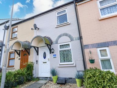 Exterior view of a row of terraced houses with small garden plants and covered porches at Kingfisher Cottage in Weymouth