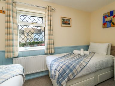 A bedroom with two single beds covered with blue plaid blankets next to a window with plaid curtains at Kingfisher Cottage in Weymouth