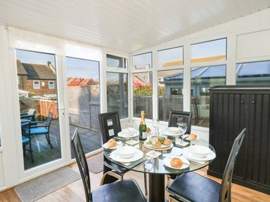 A dining area with a glass table set with plates glasses and bread rolls next to large windows at Kingfisher Cottage in Weymouth