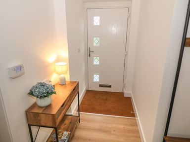 An entryway with a wooden table holding a lamp and flowers next to a white door at Berth in Afonwen near Criccieth