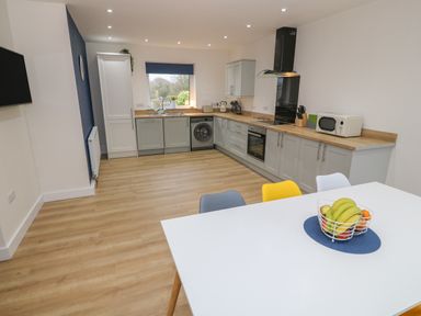 A kitchen with grey cabinets wooden countertops a white dining table with colorful chairs and a fruit basket at Berth in Afonwen near Criccieth