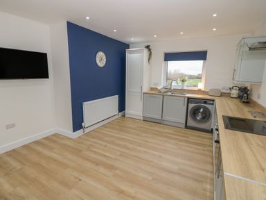 A kitchen with wooden floors and countertops gray cabinets a washing machine a wall clock and a mounted television at Berth in Afonwen near Criccieth