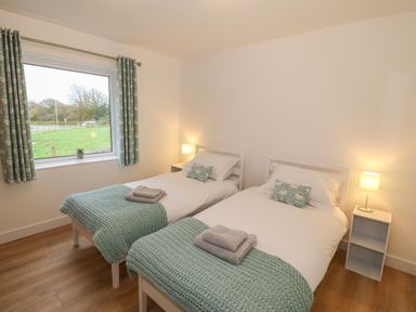 A bedroom with two single beds with teal blankets and pillows a window with teal curtains and two bedside tables with lamps at Berth Afonwen near Criccieth